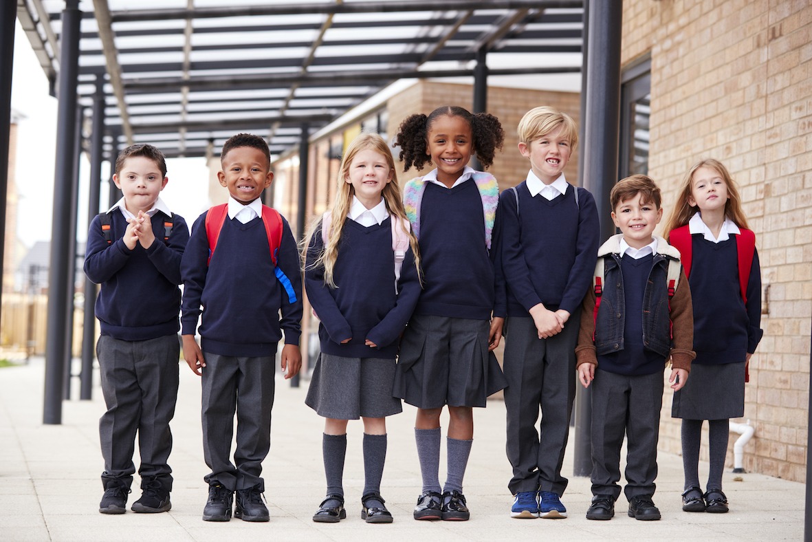 Primary school kids standing in a row on a walkway outside their school ...