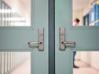 Student returning to school. School reopening by following social distancing rule after covid-19 pandemic lockdown. Locked door and handle see through blurred student lockers and student standing at background in high school or college.