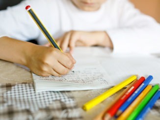 Child doing homework and writing story essay. Elementary or primary school class. Closeup of hands and colorful pencils