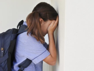 Sad young schoolgirl covering her face and crying against a wall