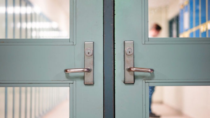 Student returning to school. School reopening by following social distancing rule after covid-19 pandemic lockdown. Locked door and handle see through blurred student lockers and student standing at background in high school or college.