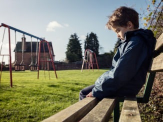 Lonely child sitting on play park playground bench