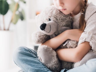 cropped shot of depressed little child embracing her teddy bear