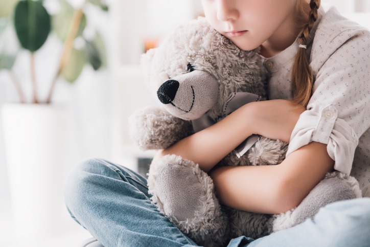 cropped shot of depressed little child embracing her teddy bear