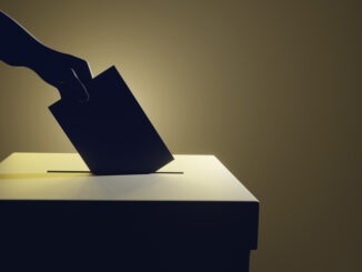 Silhouette of a hand putting a vote into the voting box on pale yellow background