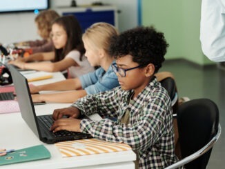 Side view of youthful African American schoolboy working in front of laptop