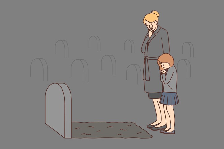 Depressed young mother and daughter crying at tombstone of deceased husband and father.