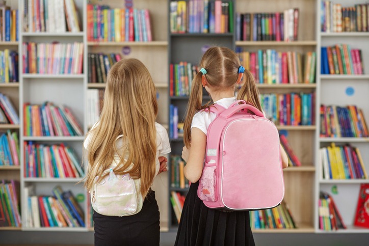 Two children choose books in school library. Books on shelves in bookstore. Children with backpacks.