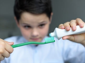 selective focus of little boy putting tooth paste on tooth brush in hand at home