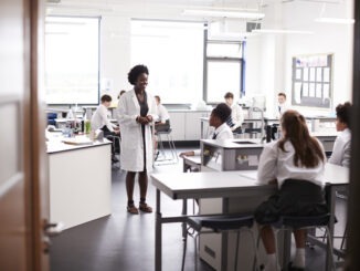 Female High School Tutor Teaching High School Students Wearing Uniforms In Science Class