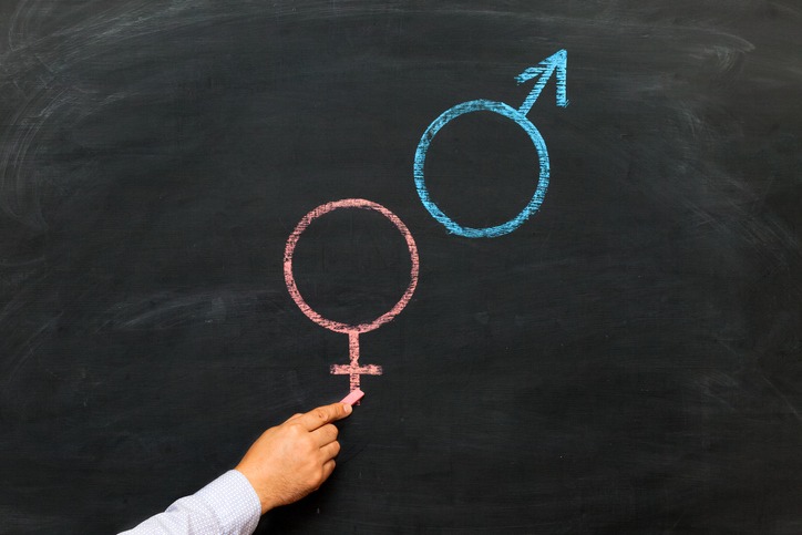 A man's hand with chalk draws a male and female gender symbol on a chalkboard