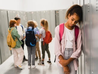Lonely sad african-american schoolgirl crying while all her classmates ignoring her. Social exclusion problem. Bullying at school concept. Racism problem