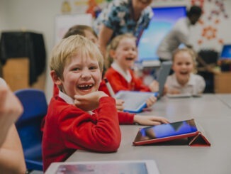 Happy little boy is smiling for the camera while using a digital tablet in his technology lesson at school.
