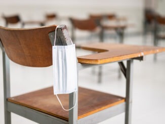 A used medical facemask hangs on a wood lecture chair in the empty classroom during the COVID-19 pandemic