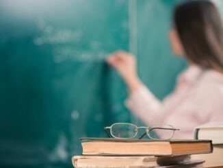 glasses and books at the classroom table while teacher writing on a blackboard