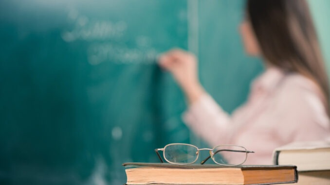 glasses and books at the classroom table while teacher writing on a blackboard