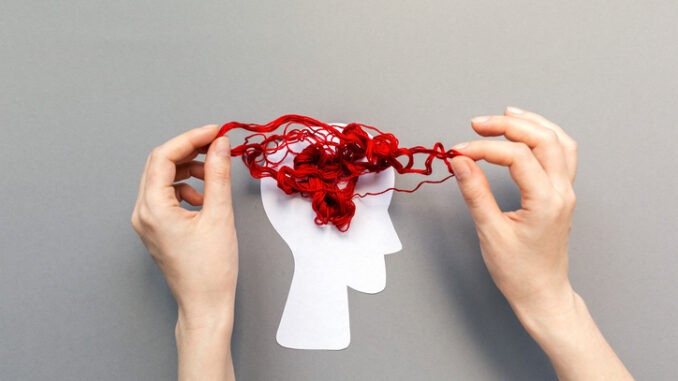 Female's hands unravel the tangled red threads on the silhouette of the head, representing the brain. Gray background. Flat lay. The concept of mental health and psyhology problem