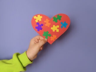 Big heart with details of puzzles in a child's hand there is a symbol of autism.