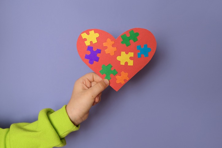 Big heart with details of puzzles in a child's hand there is a symbol of autism.