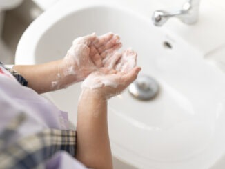 little girl in school uniform cleaning her hands with foam soap at the sink.