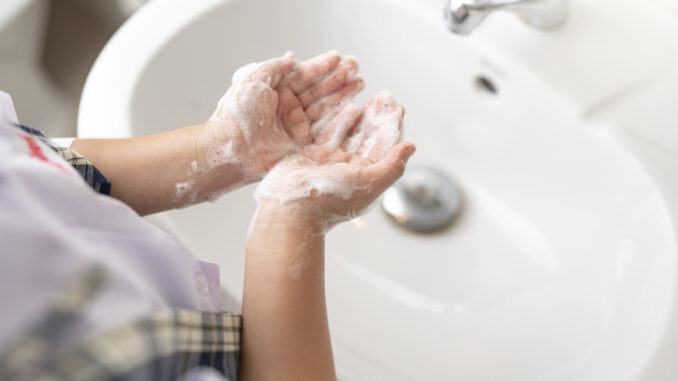 little girl in school uniform cleaning her hands with foam soap at the sink.