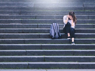 Bullying, discrimination or stress concept. Sad teenager crying in school yard. Upset young female student having anxiety. Upset victim of abuse or harassment sitting on stairs outdoors.