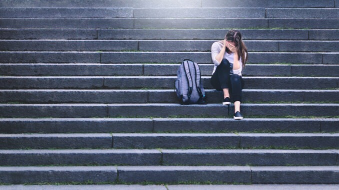 Bullying, discrimination or stress concept. Sad teenager crying in school yard. Upset young female student having anxiety. Upset victim of abuse or harassment sitting on stairs outdoors.