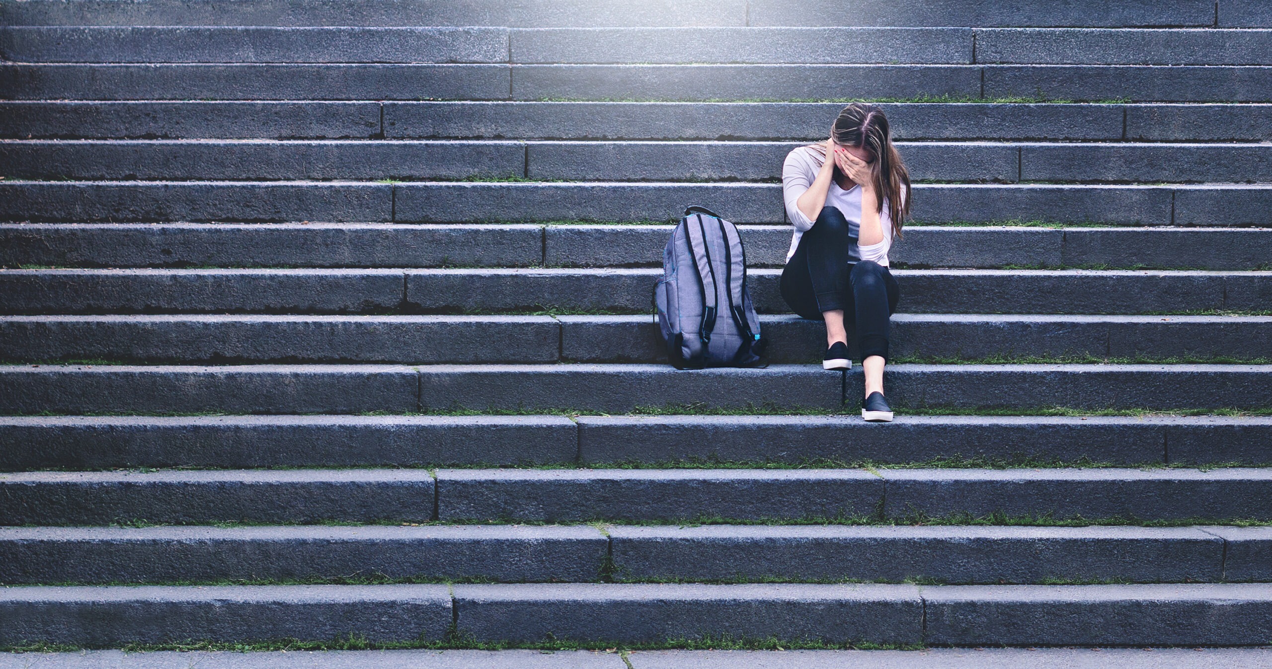 Bullying, discrimination or stress concept. Sad teenager crying in school yard. Upset young female student having anxiety. Upset victim of abuse or harassment sitting on stairs outdoors.