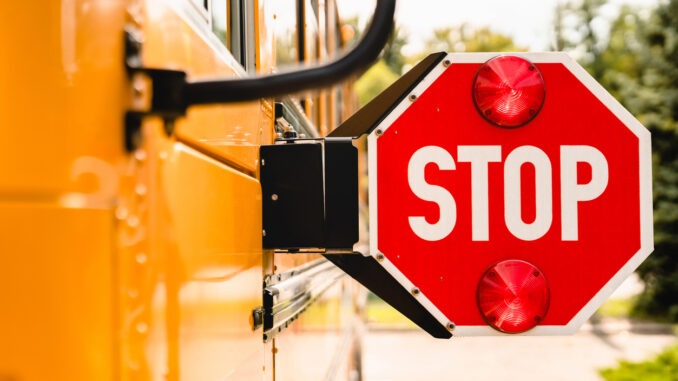 Close up yellow school bus. Stop sign. Be careful, schoolchildren crossing the road. New academic year semester. Welcome back to school. Lockdown, distance remote education learning