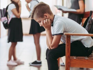 Young boy sitting alone on a bench during break at school