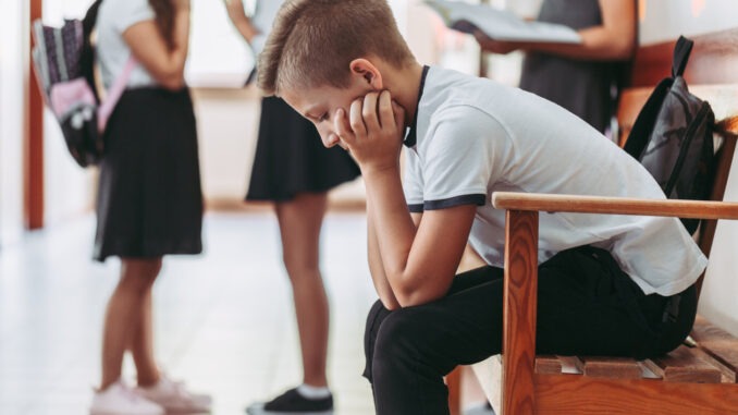 Young boy sitting alone on a bench during break at school