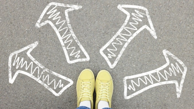 Choosing future profession. Girl standing in front of drawn signs on asphalt, top view. Arrows pointing in different directions symbolizing diversity of opportunities