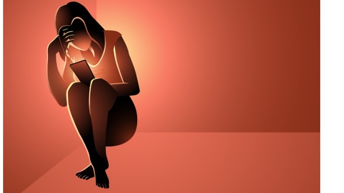 Depressed woman sitting in a corner holding a smart phone