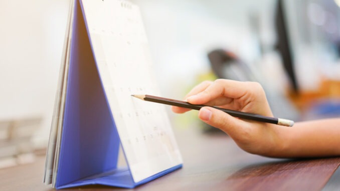 close up on woman hand with pen writing on calender for note or make appointment concept.