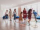 Small nursery school children with female teacher on floor indoors in classroom, doing exercise. Jumping over hula hoop circles track on the floor.