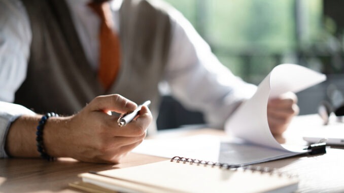 Businessman hands holding pen for working with stack of paper files, searching information, business report