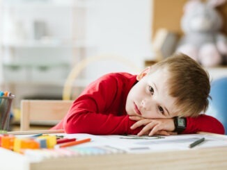 Sad little boy in red sweater feeling lonely and lying on a table