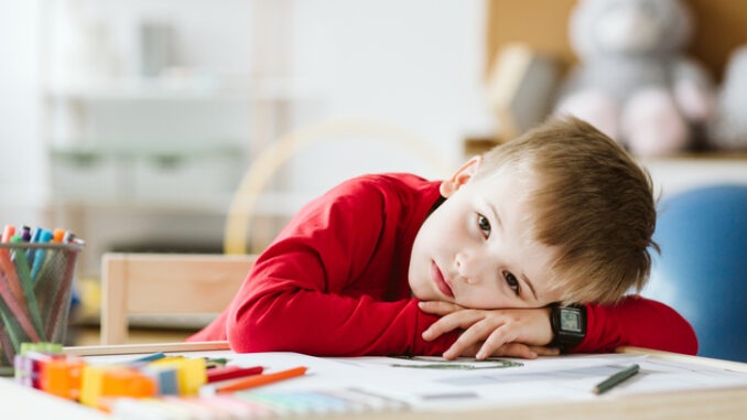 Sad little boy in red sweater feeling lonely and lying on a table