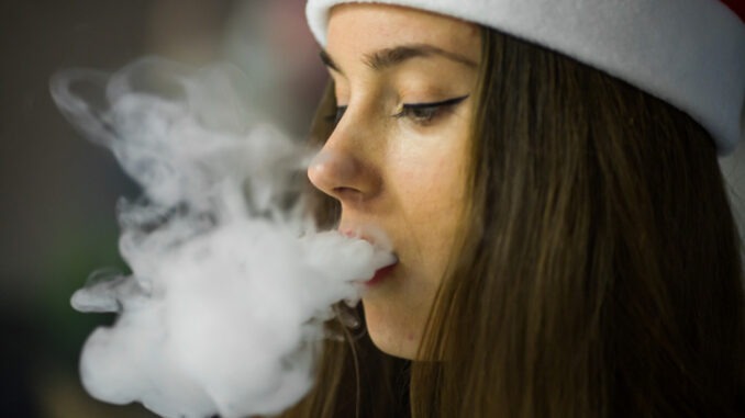 Vape teenager. Young girl in a hat smoking an electronic cigarette 