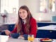 Portrait Of Smiling Teenage Girl Wearing School Uniform In Kitchen Eating Healthy Breakfast