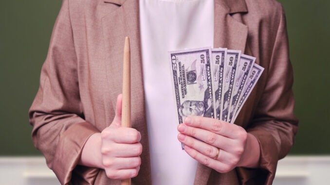 Woman teacher holding money in bills of 50 dollars in her hands on a school blackboard in the classroom