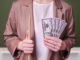 Woman teacher holding money in bills of 50 dollars in her hands on a school blackboard in the classroom