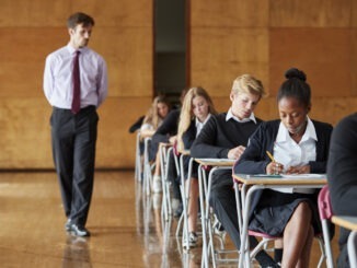 Teenage Students Sitting Examination With Teacher Invigilating