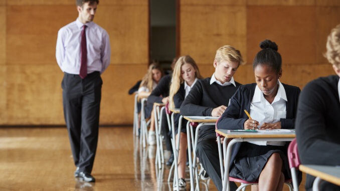 Teenage Students Sitting Examination With Teacher Invigilating