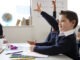 Schoolboy with Down syndrome sitting at a desk raising his hand in a primary school class, close up, side view