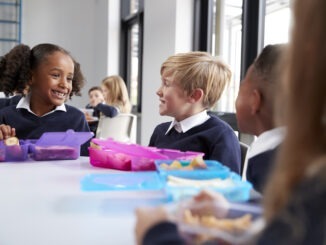 Primary school kids sitting at table eating breakfast