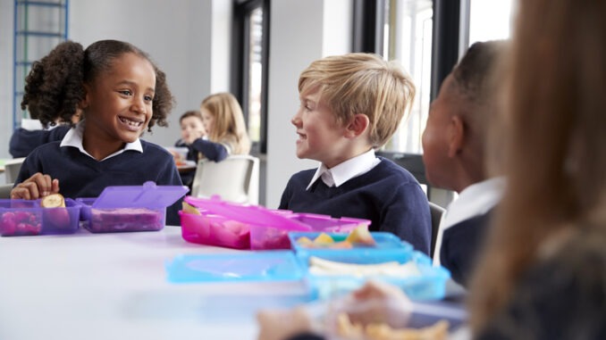 Primary school kids sitting at table eating breakfast