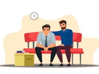 Depressed man sits at sofa, colleague support, belongings in box.