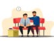 Depressed man sits at sofa, colleague support, belongings in box.