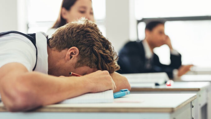 Bored male high school student sleeping during the lecture in the classroom.